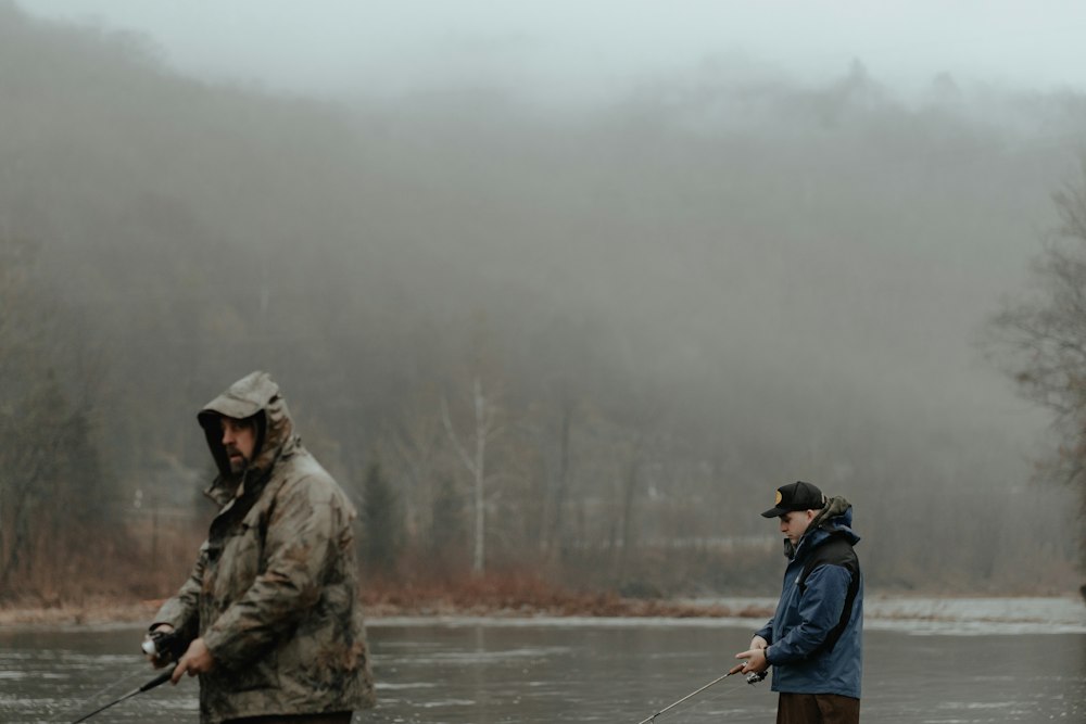 Two anglers fishing a river beneath misty wooded hills.